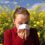 Chica estornudando en un campo de margaritas mostrando síntomas de alergia primaveral